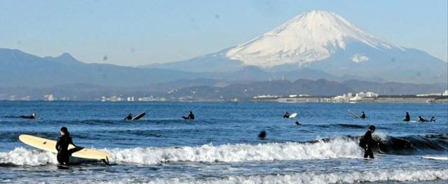 冬の富士山を背景にサーフィンを楽しむサーファーたち